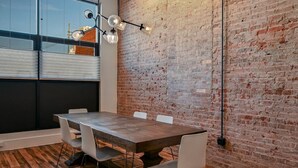 Une salle de conférence avec une table en bois, des chaises blanches, un mur en briques et un luminaire suspendu.