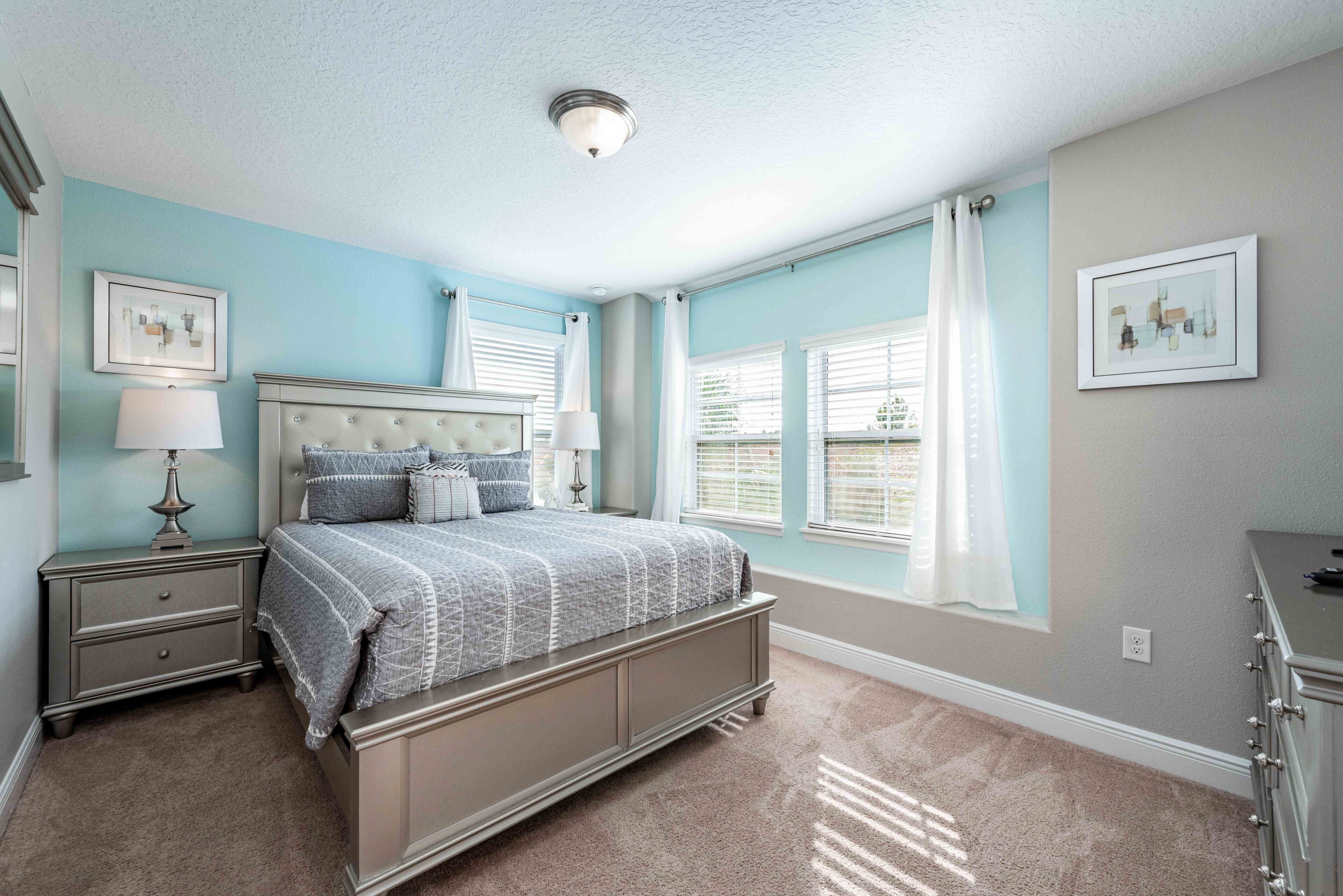 A bedroom with a bed, nightstands, a dresser, and two windows with curtains.