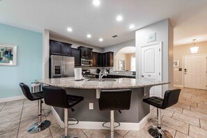 A modern kitchen with a central island, dark cabinets, stainless steel appliances, and a bar area with stools. - Modern spacious home with private pool and spa (Davenport)