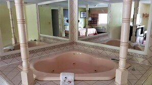 A bathroom with a large bathtub, two mirrors, and a vanity with a sink. - Royal Inn (Bellmawr)