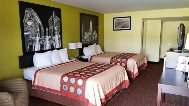 A hotel room with two beds, a desk, and a television. There are two large black-and-white photographs on the walls. - Royal Inn (Bellmawr)