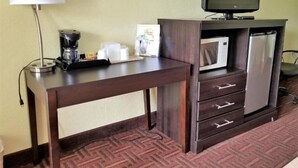 A hotel room with a wooden desk, a coffee maker, a microwave, a refrigerator, and a television. - Royal Inn (Bellmawr)