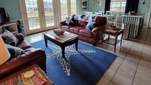 A cozy living room with a wooden ceiling, a blue rug, a leather sofa, and a dining area with a table and chairs. - Our Happy Place! (Springfield)