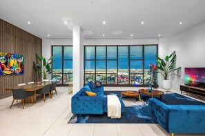 Relax in style with a panoramic city view from this spacious living room featuring a large sofa, dining area, and vibrant artwork.