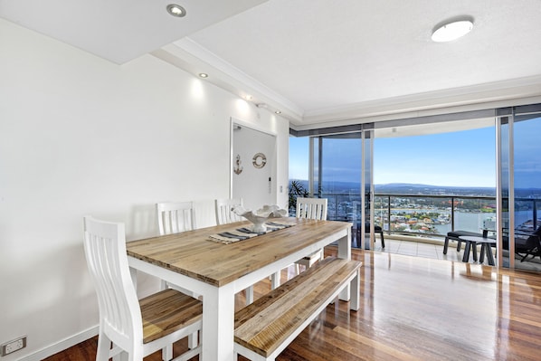 Enjoy meals in this dining area with a table and chairs, overlooking a cityscape and water view from the adjacent balcony.