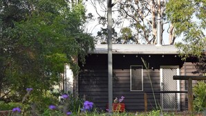 A rustic cabin with a metal roof, surrounded by dense foliage and purple flowers. - Redrock Retreat (Booie)