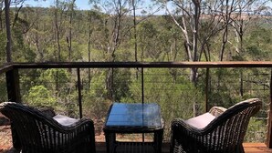 A balcony with wicker furniture and a table, overlooking a forested area. - Redrock Retreat (Booie)
