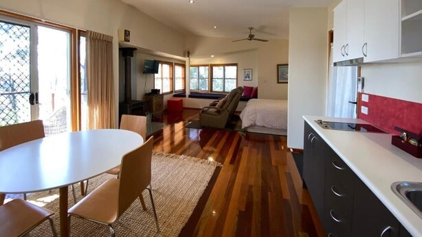 A modern kitchen with white cabinets, a dining area with a round table, and a bedroom with a bed and a window. - Redrock Retreat (Booie)