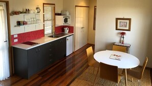 A compact kitchen with a microwave, kettle, and a small refrigerator. There is a dining area with a round table and chairs. - Redrock Retreat (Booie)
