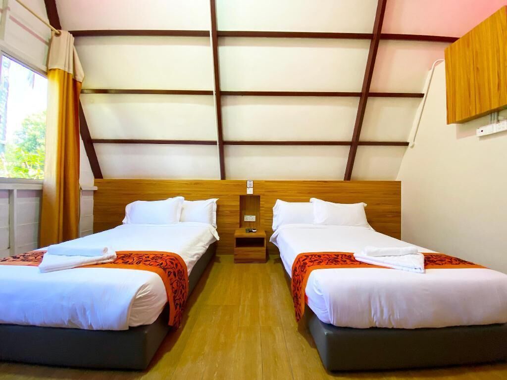 Habitación de hotel con dos camas, cabecero de madera, una mesita de noche pequeña y un ventanal con cortinas.