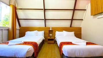 Habitación de hotel con dos camas, cabecero de madera, una mesita de noche pequeña y un ventanal con cortinas.