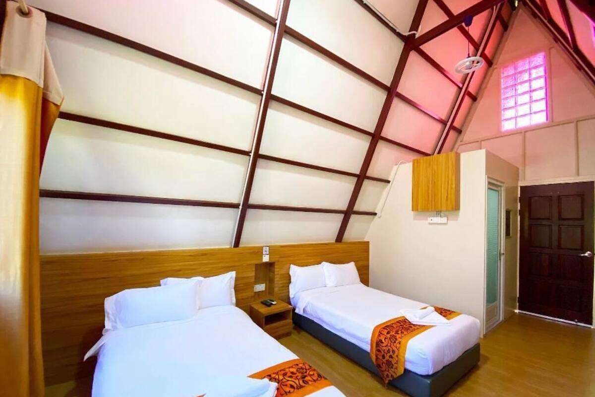 Ein Zimmer mit zwei Betten, Holz-Kopfteilen, Holzboden, einem kleinen Nachttisch mit Telefon und einer Tür mit Fenster.