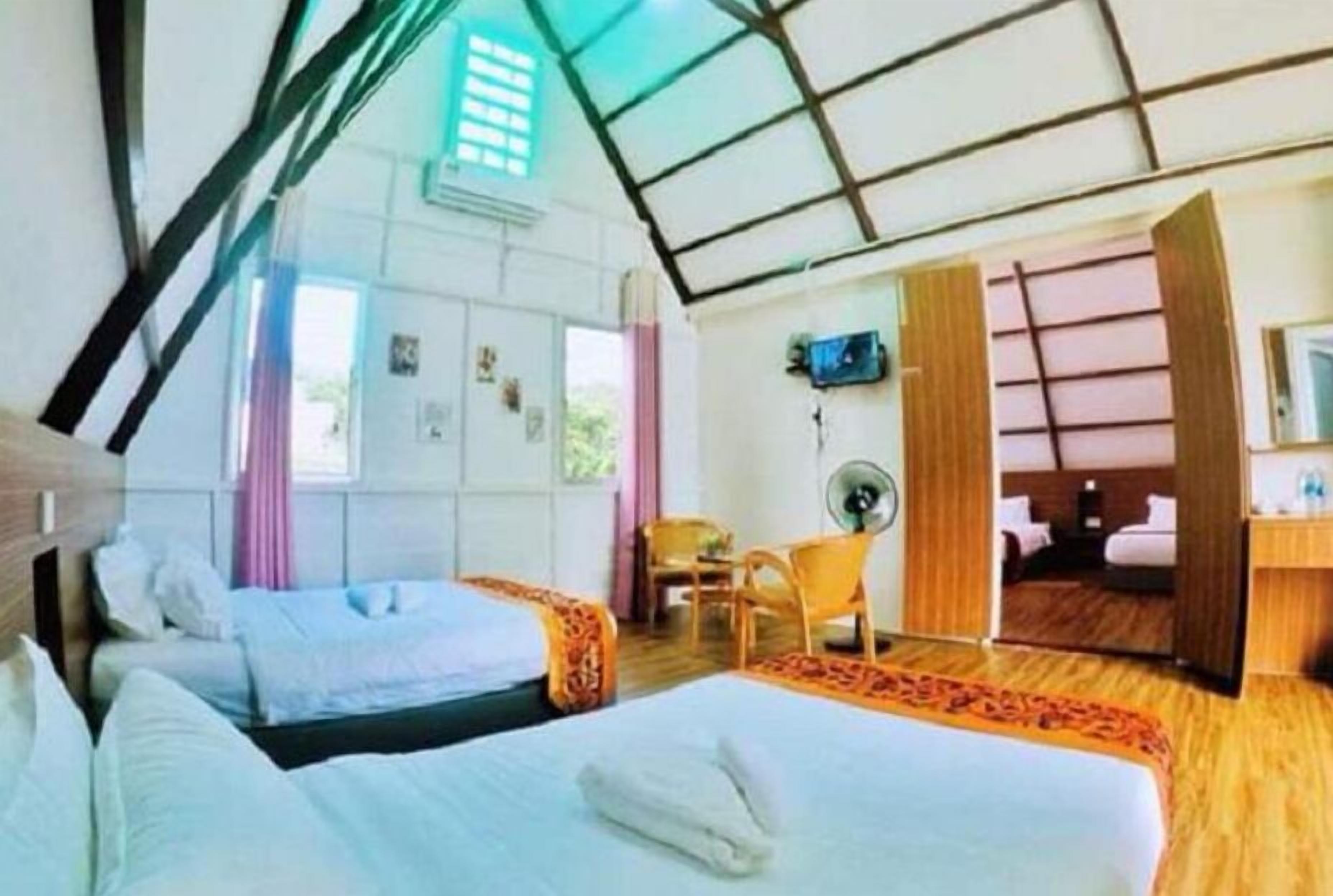Una habitación de hotel con dos camas, un escritorio, una silla y un ventilador.