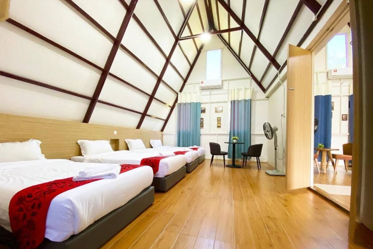 Ein Hotelzimmer mit drei Betten, Holzboden, einem Essbereich mit Tisch und Stühlen sowie Blick ins Freie durch eine Tür.