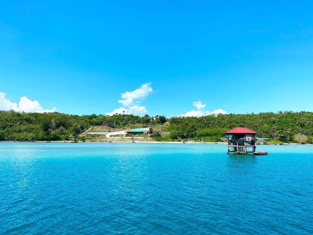 A clear blue water body with a floating structure featuring a red roof.