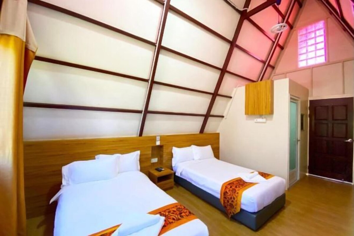Una habitación con dos camas, cabeceros de madera, una mesita de noche con lámpara y una ventana con vista al exterior.