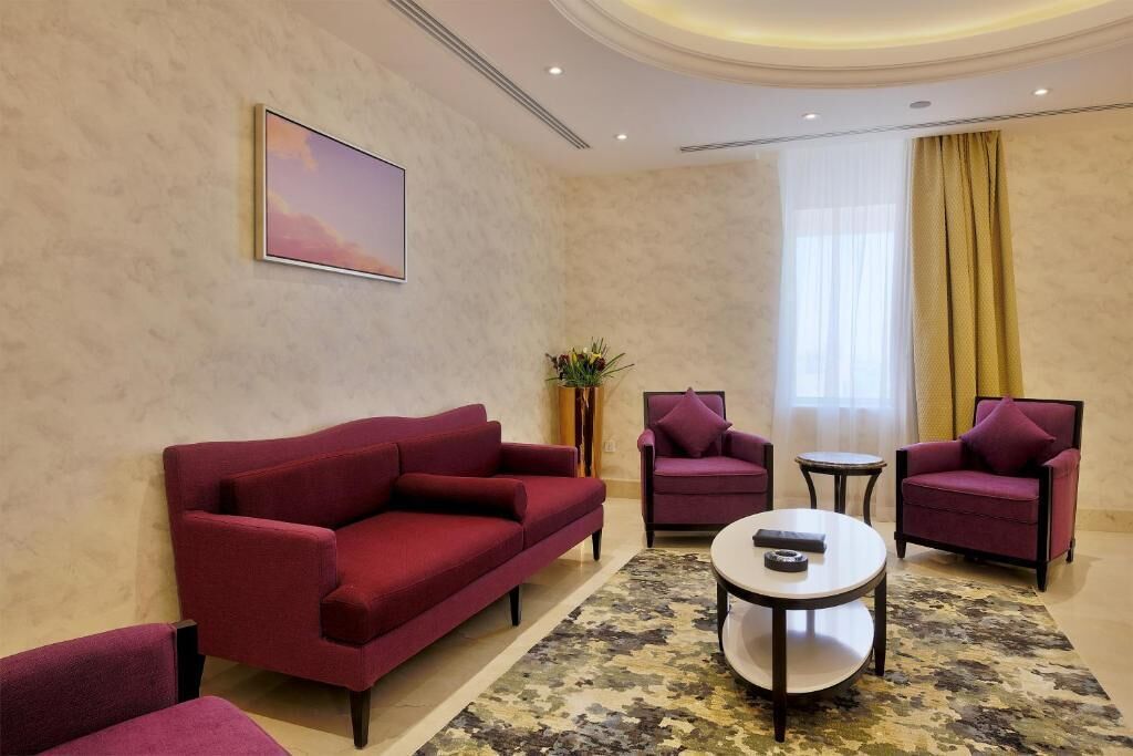 A modern lounge area with a red sofa, two armchairs, a coffee table, and a painting on the wall.