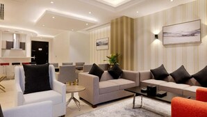 A modern living room with a sofa set, armchairs, and a coffee table. There is a painting on the wall and a plant on the side table. - The Proud Hotel (Al Khobar)