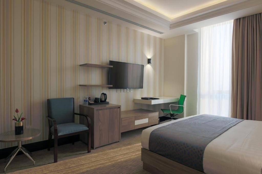 A hotel room with a bed, a desk, a chair, a TV, and a window with curtains.