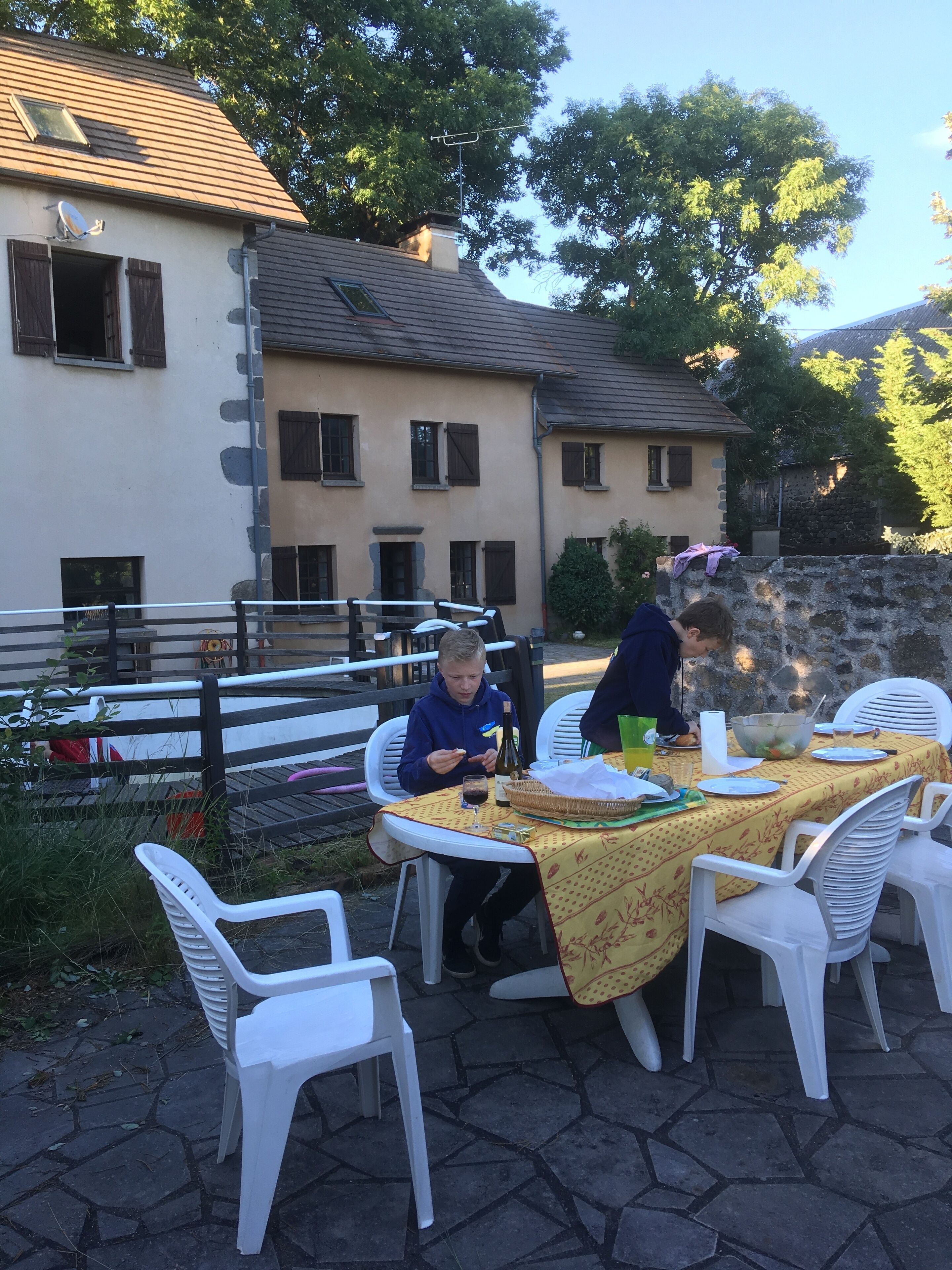 Un área de comedor al aire libre con sillas de plástico blanco y una mesa cubierta con un mantel amarillo.