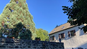 Eine Steinsäule, ein großer Nadelbaum und ein Gebäude mit einem Ziegeldach und Fenstern.