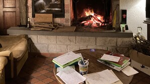 Ein Kamin aus Stein mit Fernseher, brennendes Feuer und ein unordentlicher Tisch mit Papieren und Büchern.
