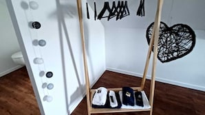 Habitación de esquina con un zapatero de madera que contiene varios pares de zapatos, una pared blanca con un adorno en forma de corazón y una pizarra con decoraciones circulares.