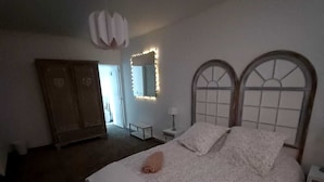Un dormitorio con una cama grande, un armario, un espejo con iluminación y una puerta que da a otra habitación.
