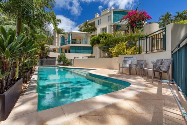 A swimming pool with a curved edge, surrounded by a tiled deck and lounge chairs. - Villa Nette - ocean views, walk to beach & restaurants, National Park (Noosa Heads)