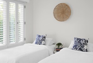 A bedroom with two beds, white bedding, and a woven wall hanging. - Villa Nette - ocean views, walk to beach & restaurants, National Park (Noosa Heads)