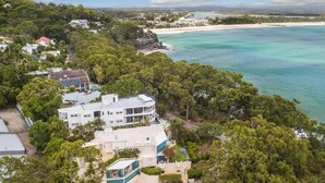 Eine Vogelperspektive zeigt ein Küstenanwesen mit einem großen Haus, umgeben von dichter Vegetation, einem Swimmingpool und einem Strand im Hintergrund.