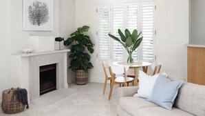 Ein Wohnzimmer mit Kamin, einem Esstisch mit Stühlen, einer Couch und einem großen Fenster mit Rollläden.