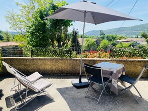 A patio with a table and chairs, an umbrella, and a view of greenery and buildings.