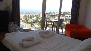 Quarto de hotel com cama, cadeira, mesa e varanda com vista para a cidade.