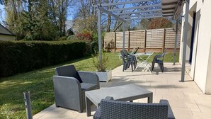 Een terras buiten met wicker meubilair, een pergola en een houten omheining.