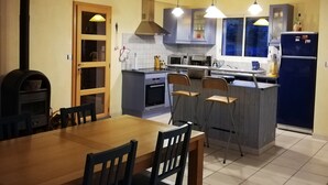 Een moderne keuken met een eethoek, met een centraal kookeiland, hanglampen en een inbouwoven.
