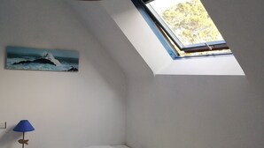 Een slaapkamer met een schuine kap, een enkel bed, een nachtkastje, een lamp, een schilderij van een vuurtoren en een dakraam.