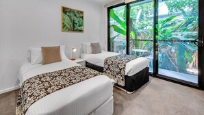 A hotel room with two beds, a ceiling fan, a large window with a view of greenery, and a framed picture on the wall. - Modern, chic 3BR townhouse in luxury complex, top location, free wifi (Bulimba)