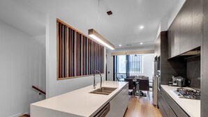 A modern kitchen with a central island, wooden slat wall, and a dining area with a view. - Modern, chic 3BR townhouse in luxury complex, top location, free wifi (Bulimba)