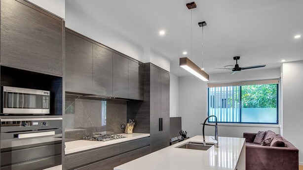 A modern kitchen with built-in appliances, a central island, and a window with a view of greenery. - Modern, chic 3BR townhouse in luxury complex, top location, free wifi (Bulimba)
