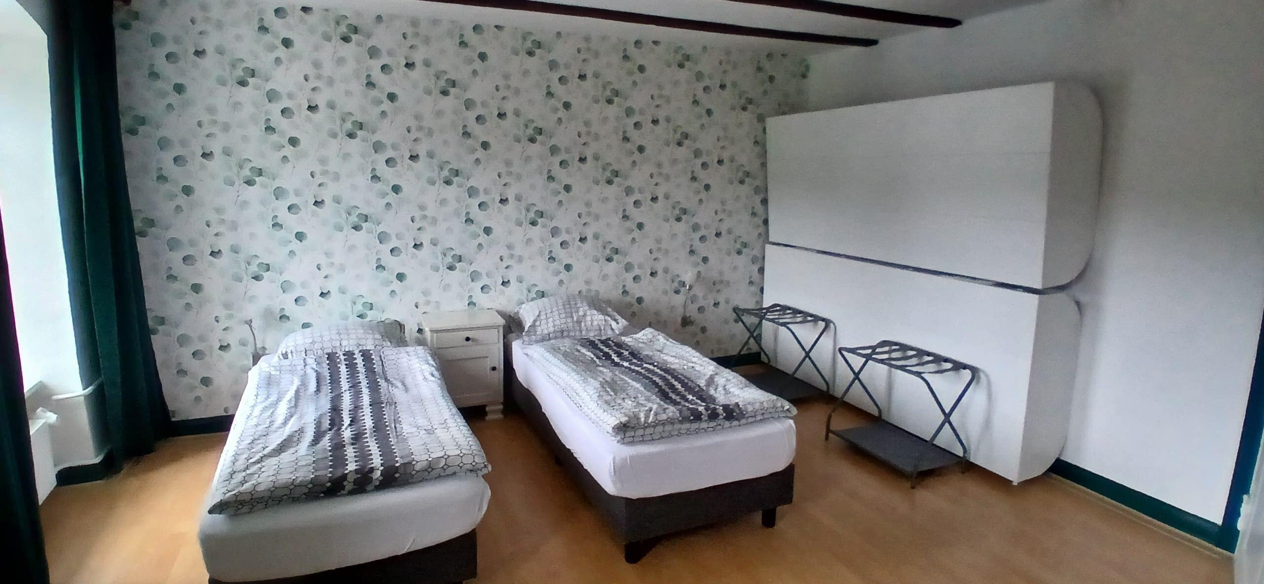 Una habitación pequeña con dos camas, un armario blanco y un televisor en la pared.