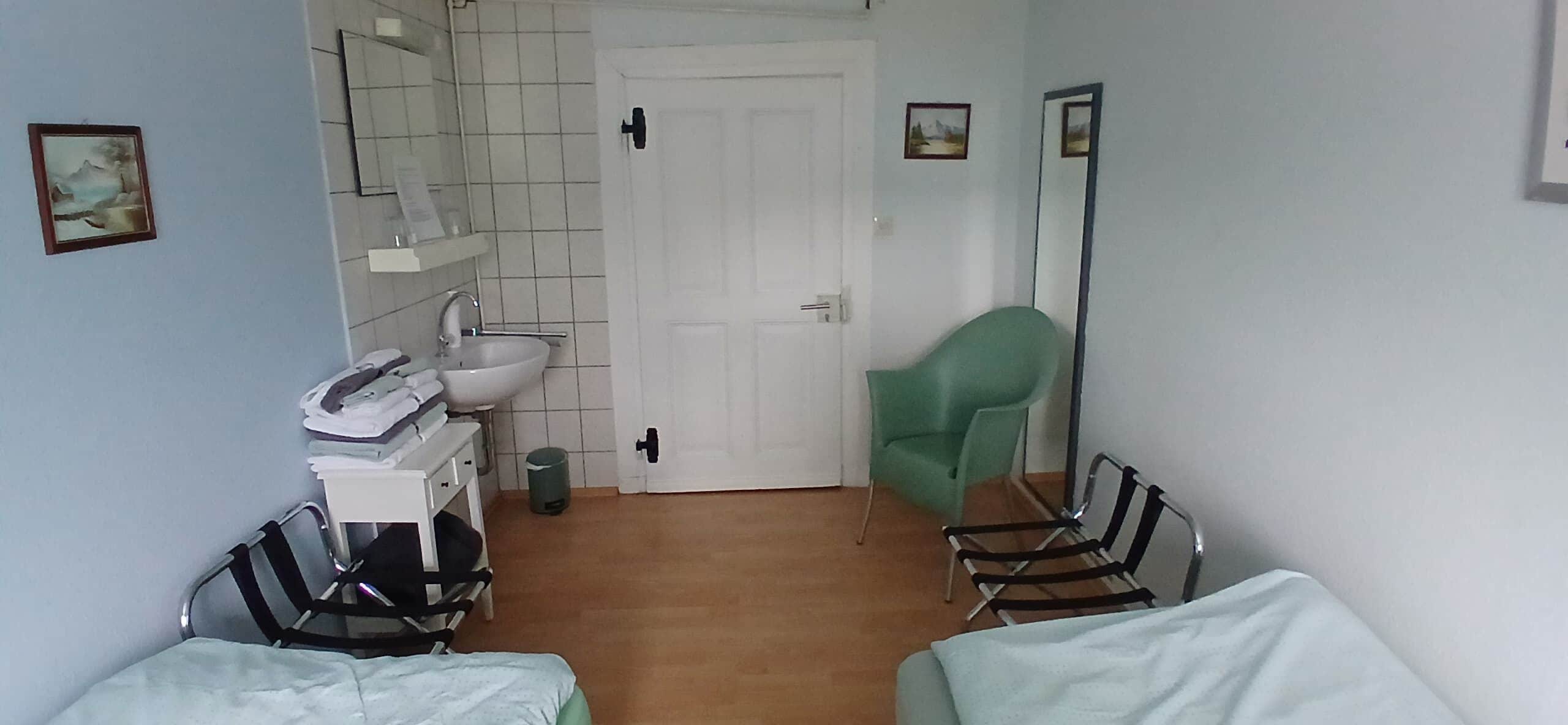 A hotel room with a bed, a chair, a small table, a mirror, a sink, and a door.