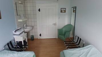 A hotel room with a bed, a chair, a small table, a mirror, a sink, and a door.