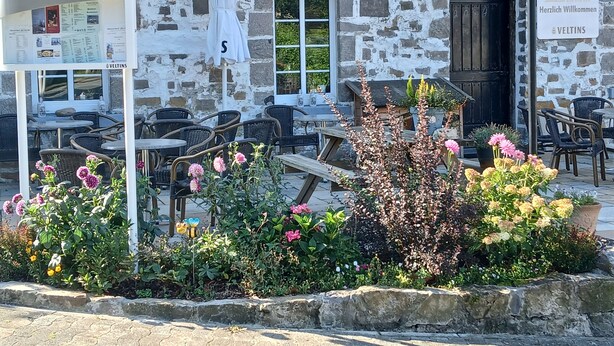 A traditional stone building with outdoor seating and a flower garden. - Gasthof Feische (Sundern)