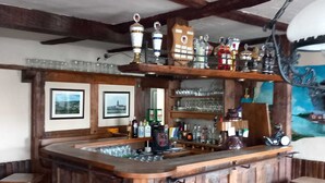 A bar area with wooden stools, a bar counter, and shelves with bottles and glasses. - Gasthof Feische (Sundern)
