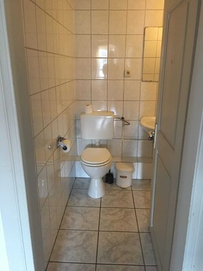 A small, tiled bathroom with a toilet, bidet, and a trash bin. - Gasthof Feische (Sundern)