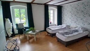 A room with two beds, a small table with a plant, a chair, and a window with curtains. - Gasthof Feische (Sundern)