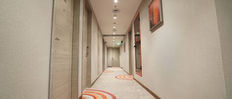 A hotel hallway with a carpeted floor, doors on the left, and a framed picture on the right wall.