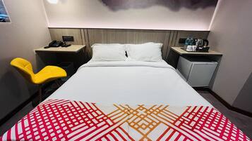Une chambre d’hôtel comprenant un lit, un bureau, une chaise, une table de chevet et une lampe fixée au mur.