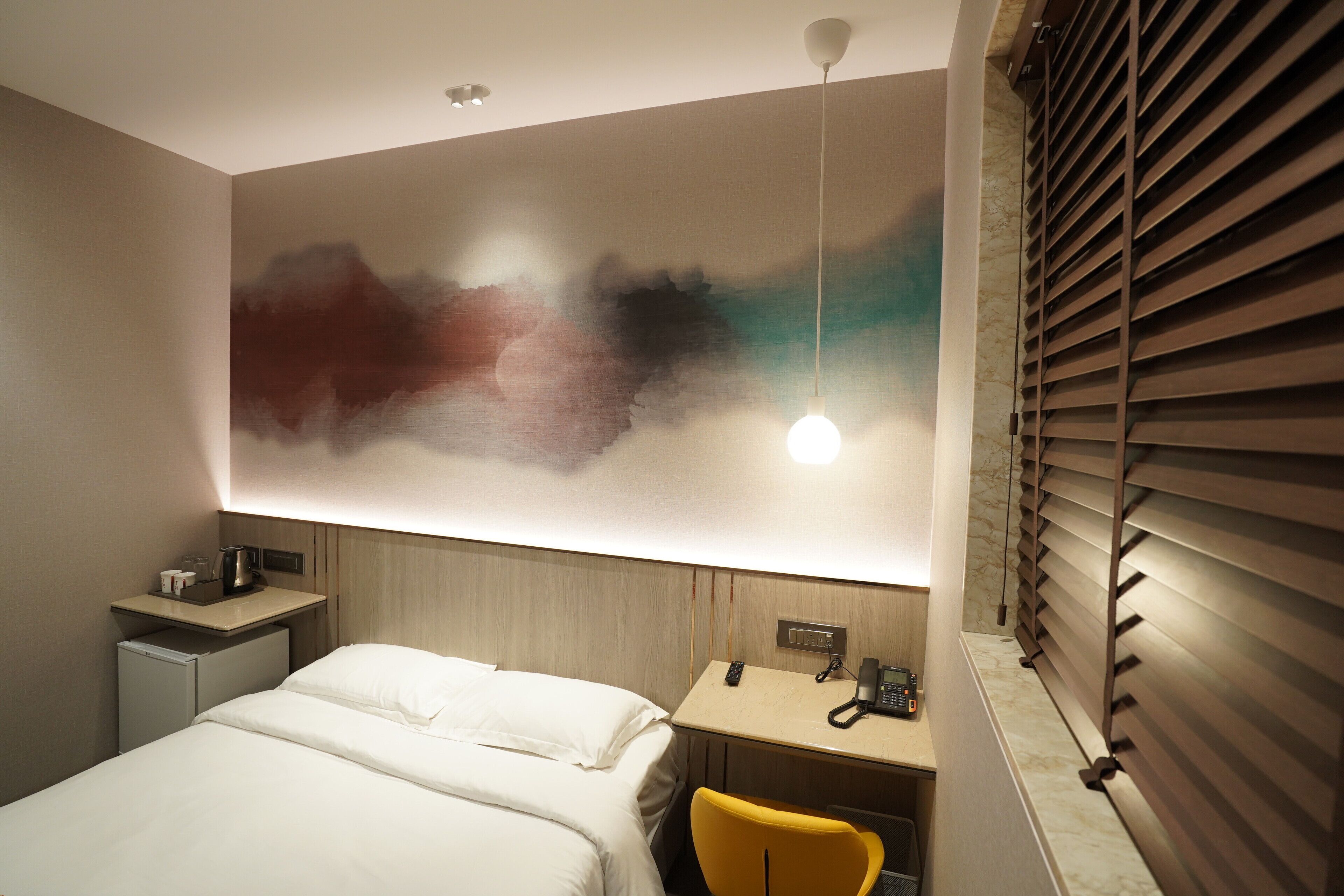 Une chambre d’hôtel comprenant un lit, un bureau avec un téléphone, un petit réfrigérateur et une œuvre d’art accrochée au mur.